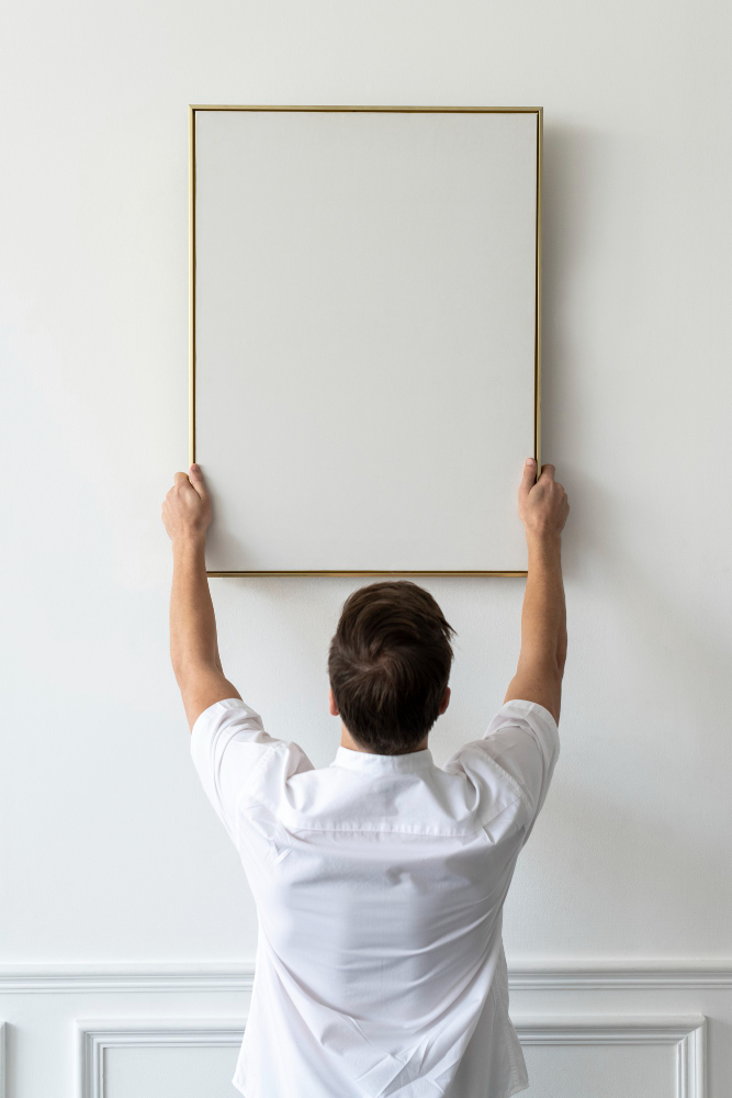 un homme qui accroche un tableau sur un mur blanc