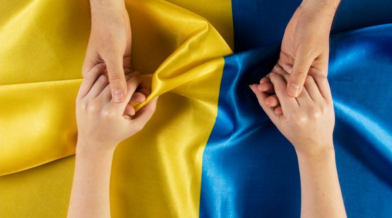 deux personnes se tenant les mains au dessus du drapeau de l'Ukraine