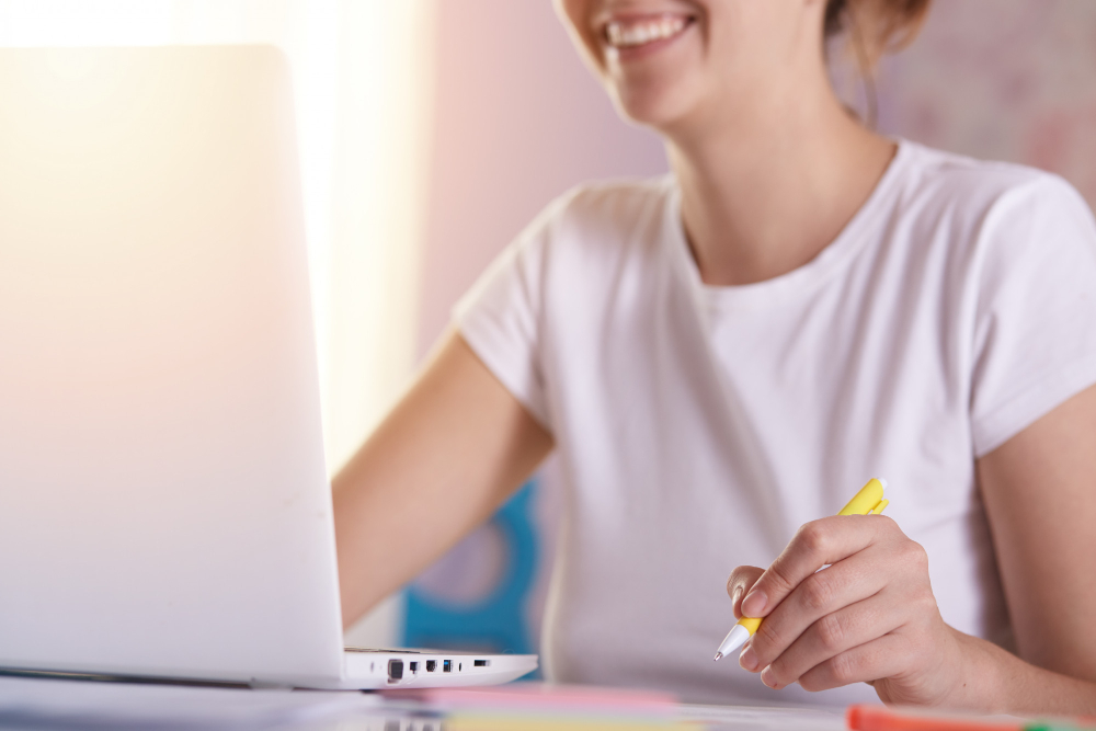 une femme qui sourit en prenant des notes devant son ordinateur
