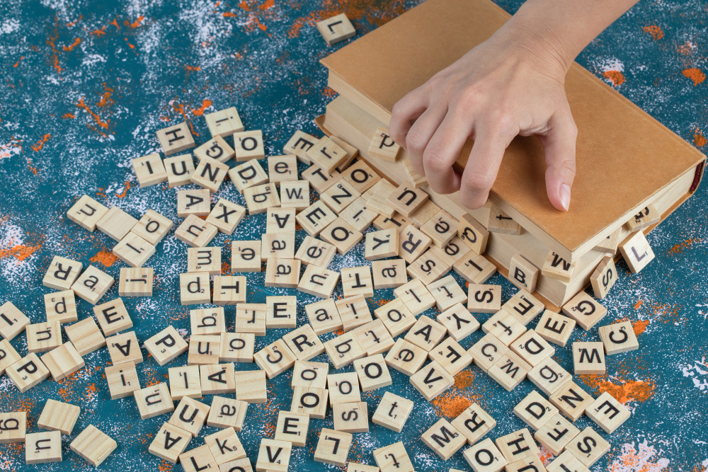 une main posé sur un livre duquel sort une multitude de jetons de scrabble